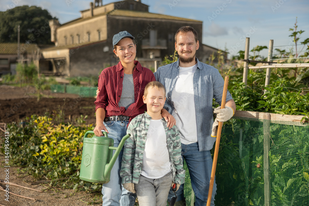 Fototapeta premium Family of farmers with garden tools in front of a vegetable garden. Generation of farmers growing organic vegetables