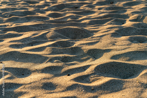 Fototapeta Naklejka Na Ścianę i Meble -  Close-up of golden hour light casting soft shadows over textured sand dunes on a quiet beach.