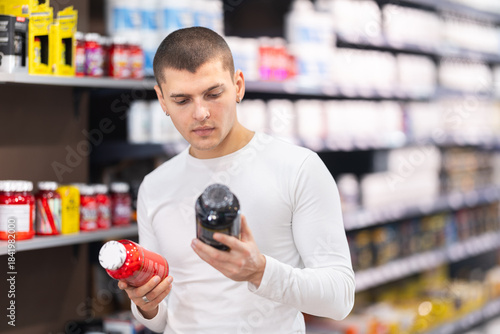 Fotografía Focused young guy choosing a bottle of vitamin supplements in large sports nutri