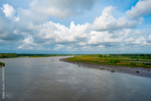 Obraz na plátně A peaceful riverscape featuring a broad waterway, green riverbanks, and a dramatic cloud-filled sky