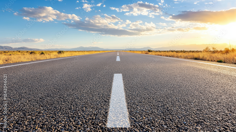 Fototapeta premium Open highway stretching toward sunlit horizon with dramatic sky and distant mountains