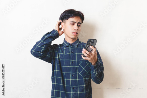 Cuadro en lienzo Frustrated young Asian man reacting to a smartphone problem, showing stress and discomfort while checking his phone