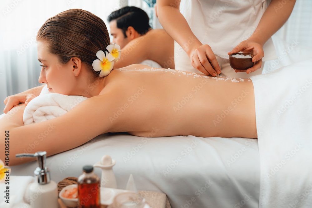 Obraz premium Blissful couple customer having exfoliation treatment in luxury spa salon with warmth candle light ambient. Salt scrub beauty treatment in health spa body scrub. Quiescent