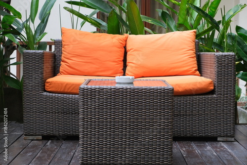 Stylish outdoor rattan sofa with vibrant orange cushions placed in a lush garden setting, creating a cozy and inviting seating area.