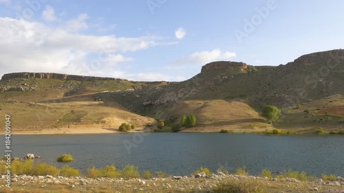 Akkoy dam creating a reservoir surrounded by arid hills and a partly cloudy sky in Turkey