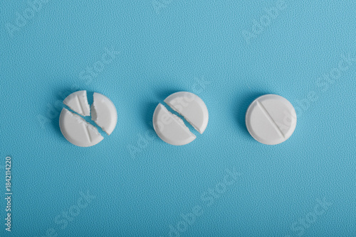 Fotografie White round tablets in different broken stages arranged in a row on a blue background, illustrating medication dosage, splitting, and pharmaceutical concepts