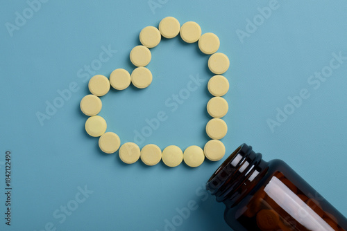 Heart shaped pills spilling from a bottle on a blue background. Top view, with space for text. Medical and healthcare concept.