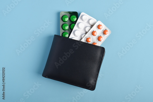 Wallet with a blister pack of pills on a blue background, top view. Concept of health care costs, medical expenses, and financial responsibility in medicine.