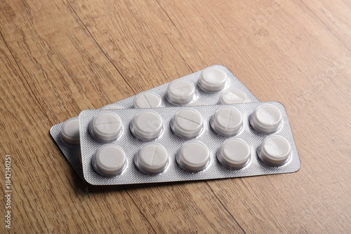 White pills in an isolated plastic blister pack on a wooden table, healthcare and medicine concept.