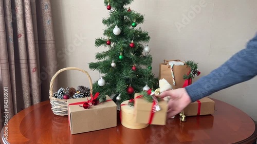 Merry Christmas and Happy New Year! This time-lapse video shows gifts in eco-friendly paper boxes with red ribbons appearing on a table next to a decorated artificial Christmas tree  in cozy home