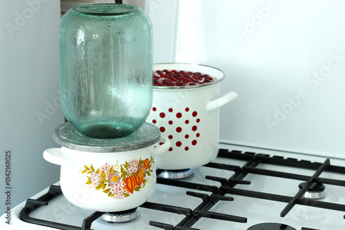 The process of sterilizing large glass jars on a gas stove in an enameled pan, preparing for rolling up cherry compote for the winter