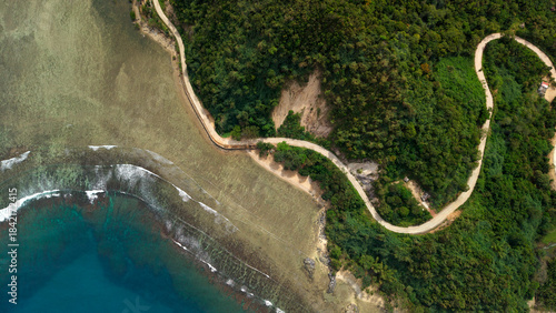 Vertical top-down drone shot of winding concrete coastal road hugging the shoreline next to turquoise coral reef in Barangay Cheey Busuanga Island Philippines