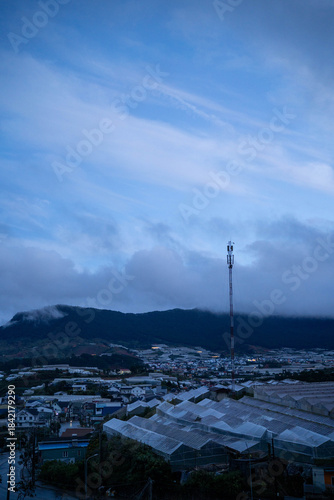 Wallpaper Mural A serene twilight view of a town with greenhouses under a blue sky and distant mountains. Torontodigital.ca