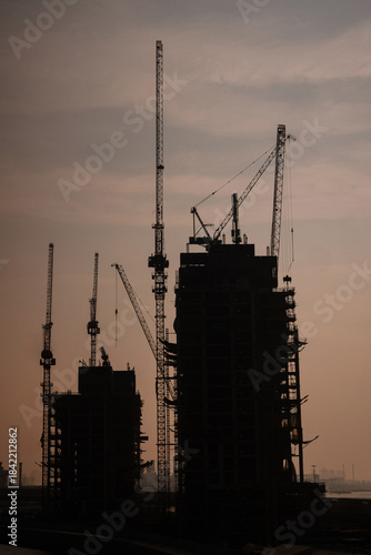 Construction site with large tower cranes against a sunset sky. Vertical image