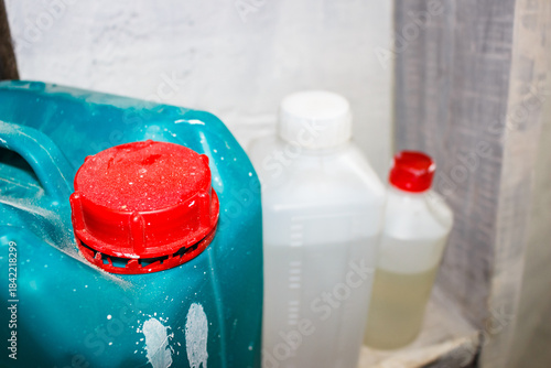 Vibrant red cap on a teal plastic jerrycan with white speckles, set against blurry background of other chemical containers