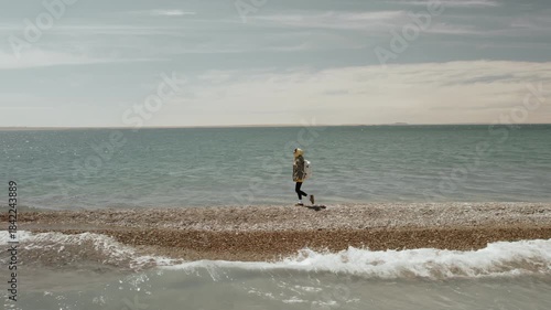 Girl trekker with a backpack walks along a spit in the middle of the endless waters of a high-mountain lake in the Gobi Desert, Mongolia. Solo travel, adventure, summer vacation, youth