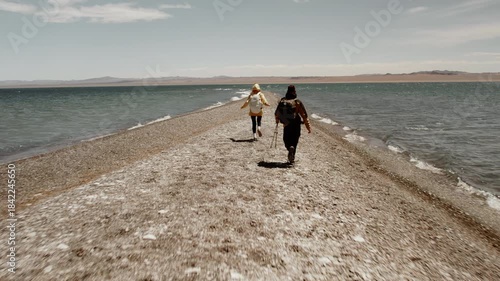 Back view of two active tourists male and female running along a spit of a lake in the high mountain desert Gobi in Mongolia, Mongol Els region. Joy, fun, wilderness travel, summer vacation