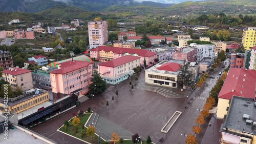 Aerial view of Abat Doçi Square in Rrëshen, Northern Albania, surrounded by colourful buildings, autumn trees and rolling hills.