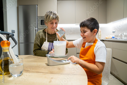 Mother and son enjoying baking together in a modern kitchen. Boy learning to weigh flour on a digital scale