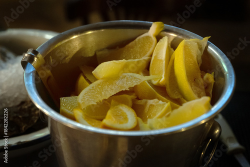 Bucket of Fresh Lemon Slices Ready for Beverage Serving. Close-up of yellow citrus fruits in a metal container, perfect for cocktails, detox, or food preparation concepts.