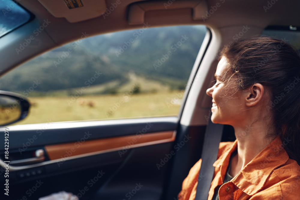 Naklejka premium Woman in an orange shirt sits as a passenger in a car, gazing through the window at a vast scenic landscape during a calm travel moment.