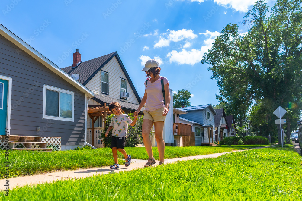 Fototapeta premium Mother and son walking on sidewalk in suburban neighborhood in drumheller, canada