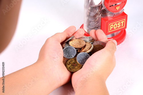 小銭を持つ子どもの手とポスト型の貯金箱