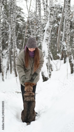 A young woman relaxes during a walk in a winter forest with her dog.
