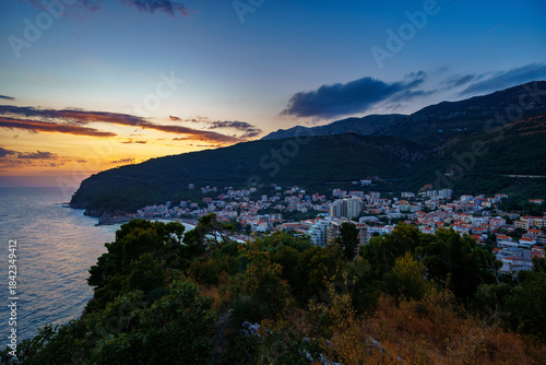 Fototapeta Naklejka Na Ścianę i Meble -  sunset in small resort town Petrovac, Montenegro, beautiful sea view, city embankment with street lights, beach and mountains against sunset sky
