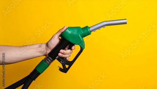Hand holding green fuel nozzle against bright yellow background.