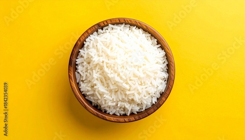 Wooden bowl of fluffy white rice on vibrant yellow background.