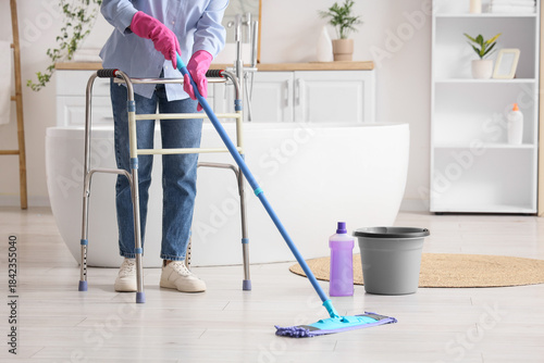 Mature woman with walker mopping floor in bathroom