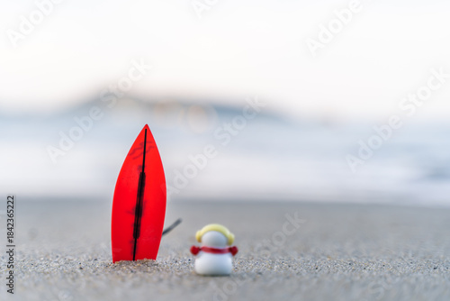 Sandy Christmas Snowman is watching the waves, standing on beautiful beach with a surf board - horizontal version in Patong Beach, Phuket, Thailand
