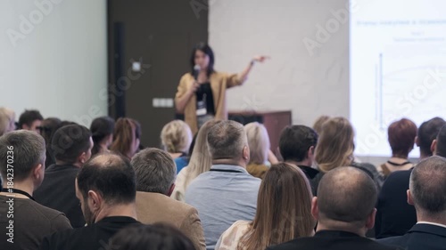 Presenter speaks to crowded room during training session audience listens notes focus leadership communication industry insights in dynamic conference setting.