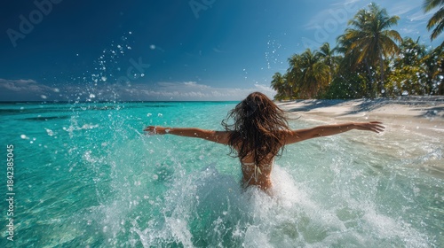 Joyful tropical beach moment: fit woman in bright bikini splashing water with open arms on a paradise shore