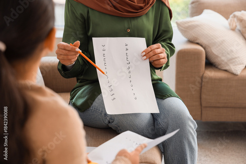 Muslim mother with her little daughter learning Arabic language on sofa at home