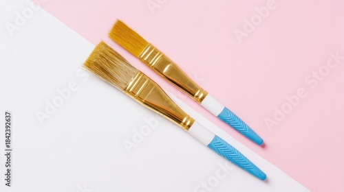 Two paintbrushes rest against a split colored white and pink background,