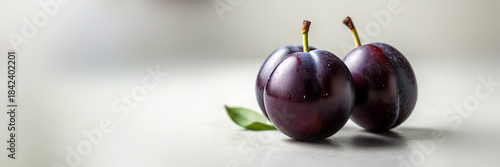 Fresh purple plums with green leaves on light background showcasing texture