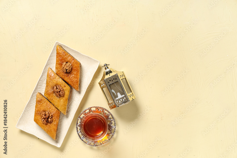 Fototapeta premium Glass of tasty Turkish tea with baklava and fanoos on beige grunge background. Ramadan celebration