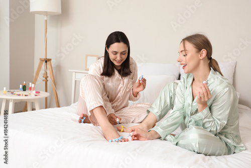 Принти на полотні Young women in pajamas with nail polishes making pedicure in bedroom