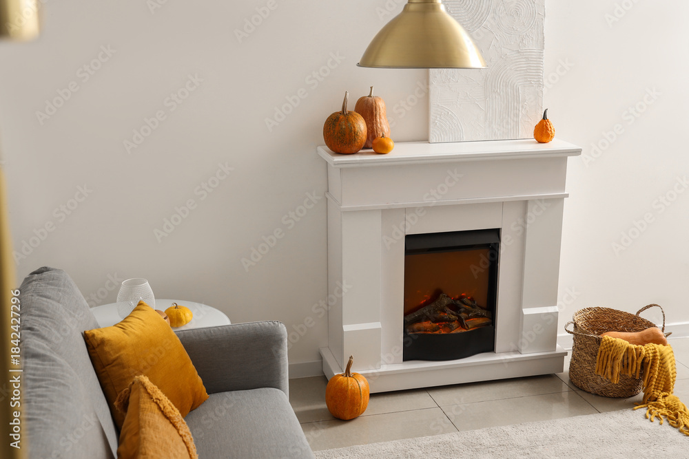 Obraz premium Autumn interior of living room with cozy grey sofa, fireplace and pumpkins