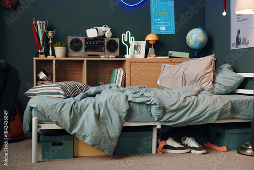 Tableau sur toile Messy bed with striped pillow and wrinkled blanket in teenager bedroom, bookshel