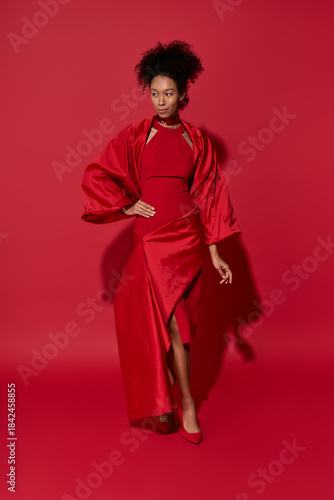 Young woman in radiant red attire exuding confidence against a bold crimson backdrop