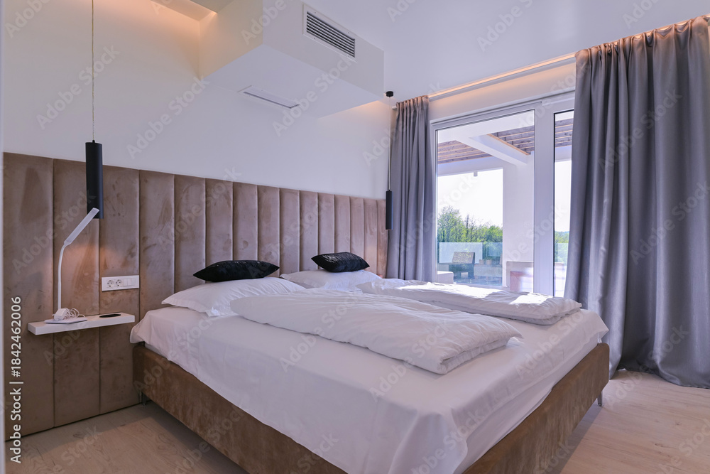Fototapeta premium Bright, modern bedroom featuring a comfortable bed, sleek desk, and a large sliding glass door opening to a private balcony with stunning green landscape views, perfect for relaxation and serene