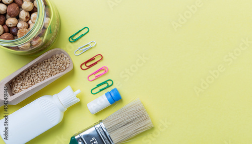 Assorted Craft Supplies Arranged on Yellow Surface Nuts, Seeds, Glue, and Brush