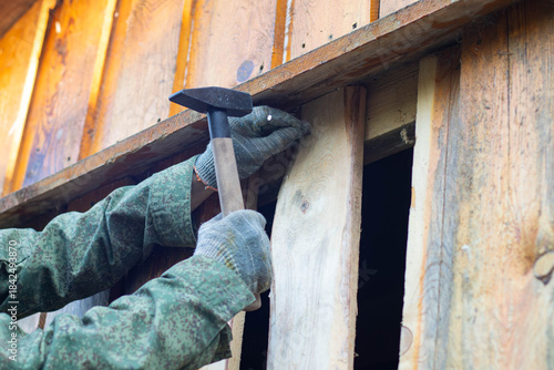 Canvas Print A close-up of a hand wearing a glove, holding a hammer to nail wooden planks on a wall