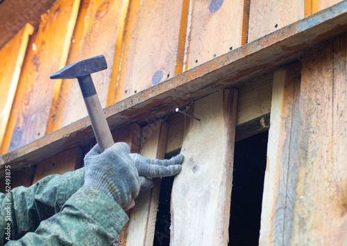 Canvas Print A close-up of a hand wearing a glove, holding a hammer to nail wooden planks on a wall