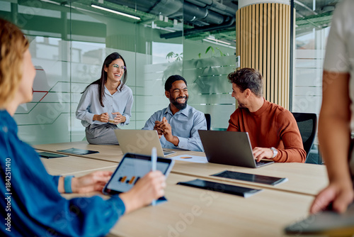Diverse business professionals sharing ideas, smiling, and using technology during a productive meeting in a modern office environment