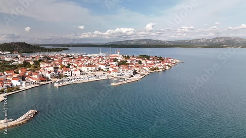 Drone rotates around old town Betina, island Murter, revealing stone houses, marina, and a wide calm-day panorama stretching across the Adriatic toward the Croatian mainland.