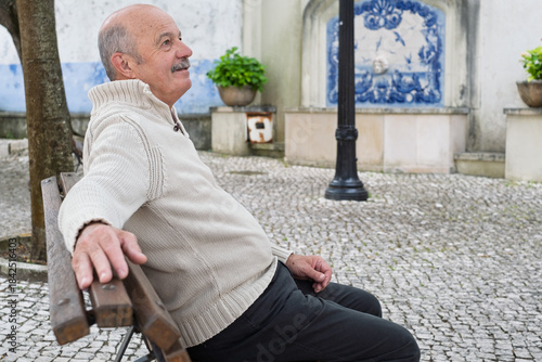 An elderly Spanish man is resting while sitting on a bench, enjoying a quiet moment outdoors 